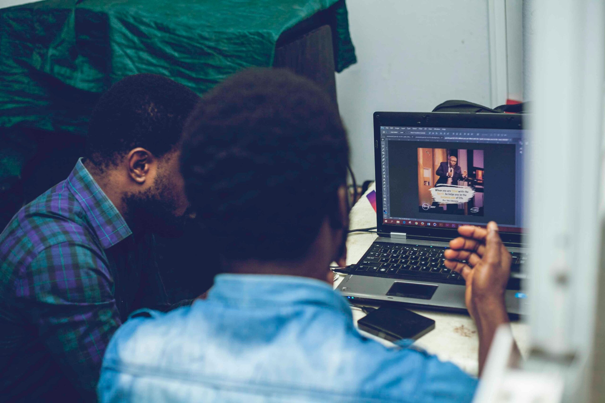 Two men collaborating on graphic design using a laptop indoors, focusing on technology and teamwork.